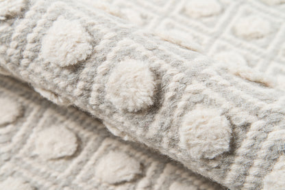 Close-up of a gray and ivory rug with raised circular pom-poms and plush woven texture.