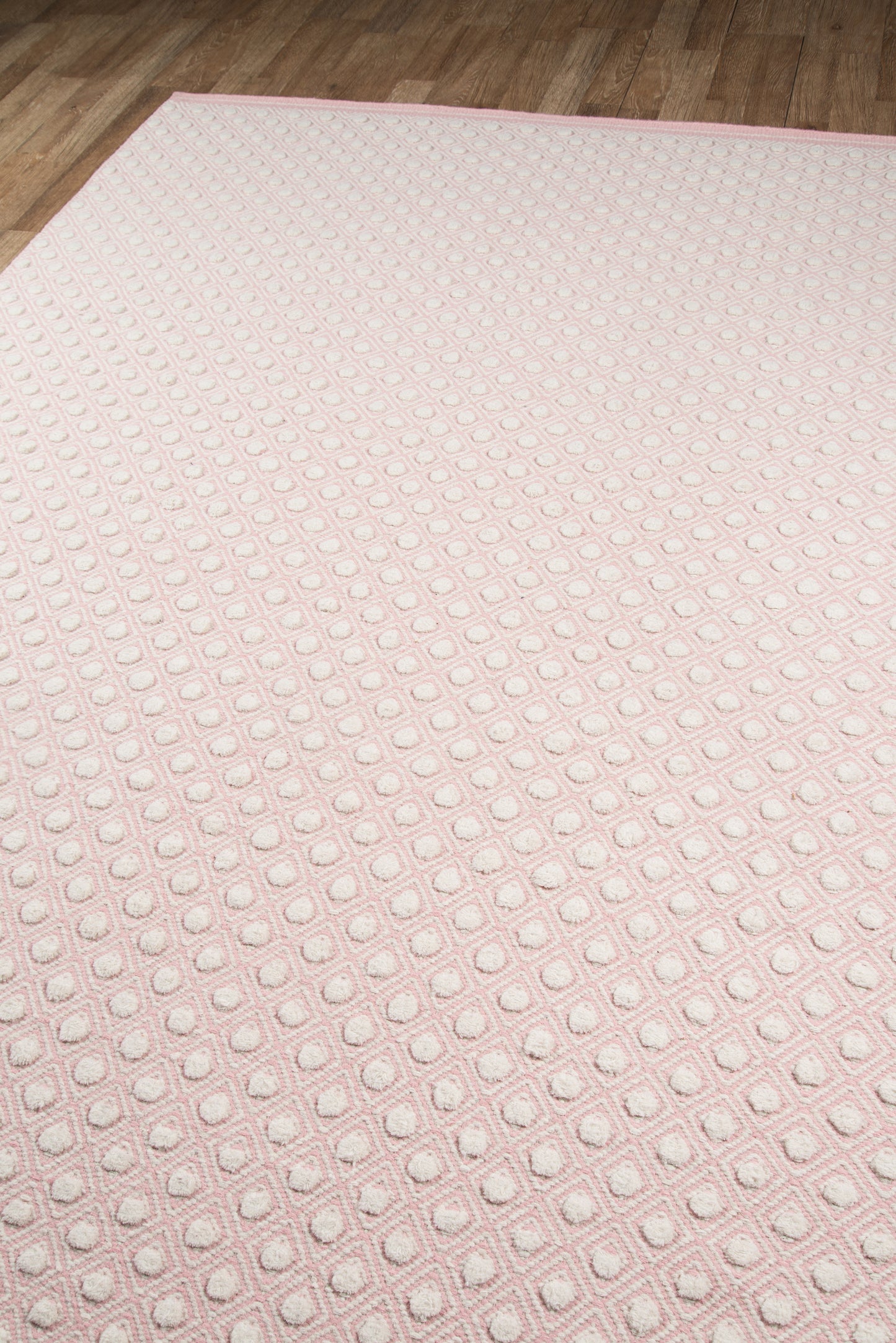 Soft pink rug with a raised dot grid in square outlines on a wood floor.
