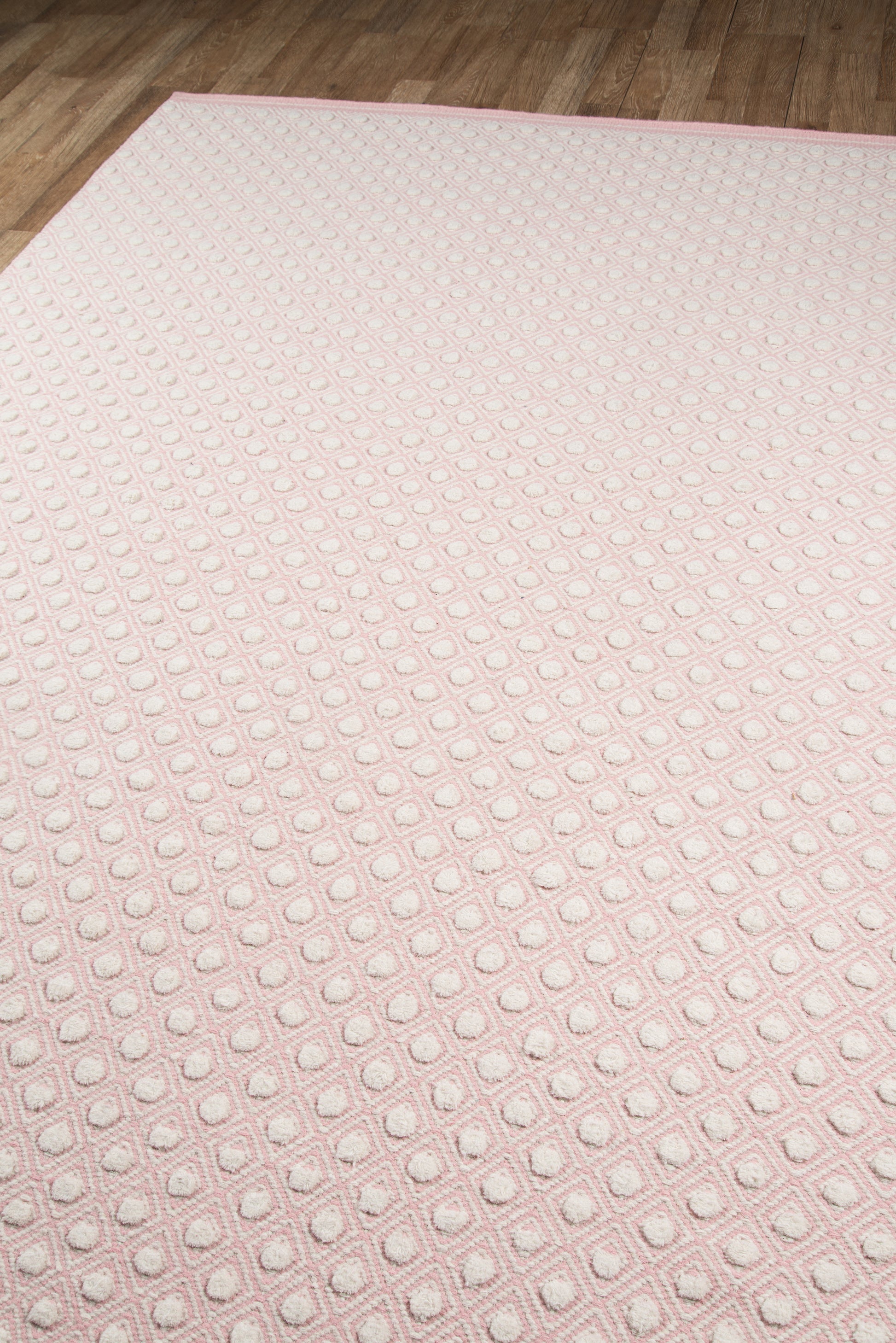 Soft pink rug with raised square grid pattern, plush texture, rectangular shape on a wooden floor.