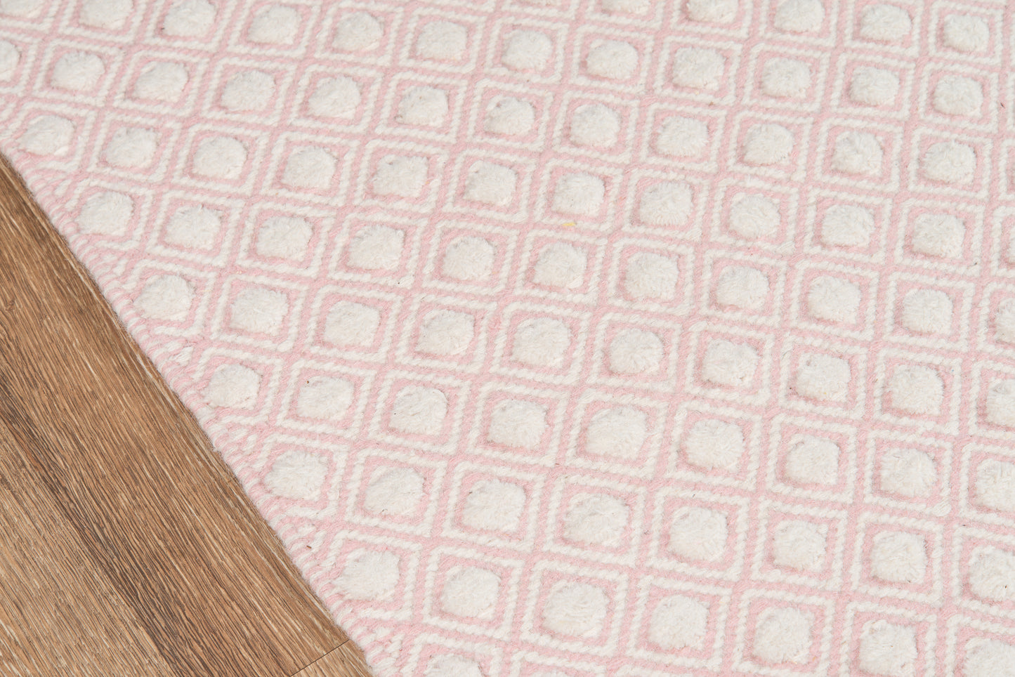 Soft pink tufted rug with white square grid pattern on a light wood floor.
