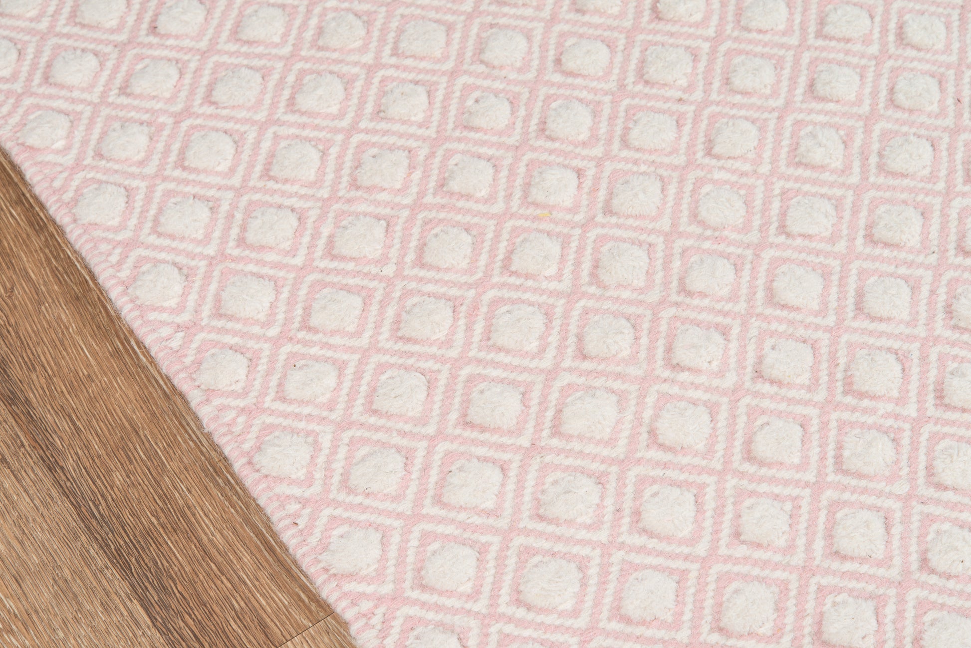 Pink patterned rug with white square motif on a wooden floor.