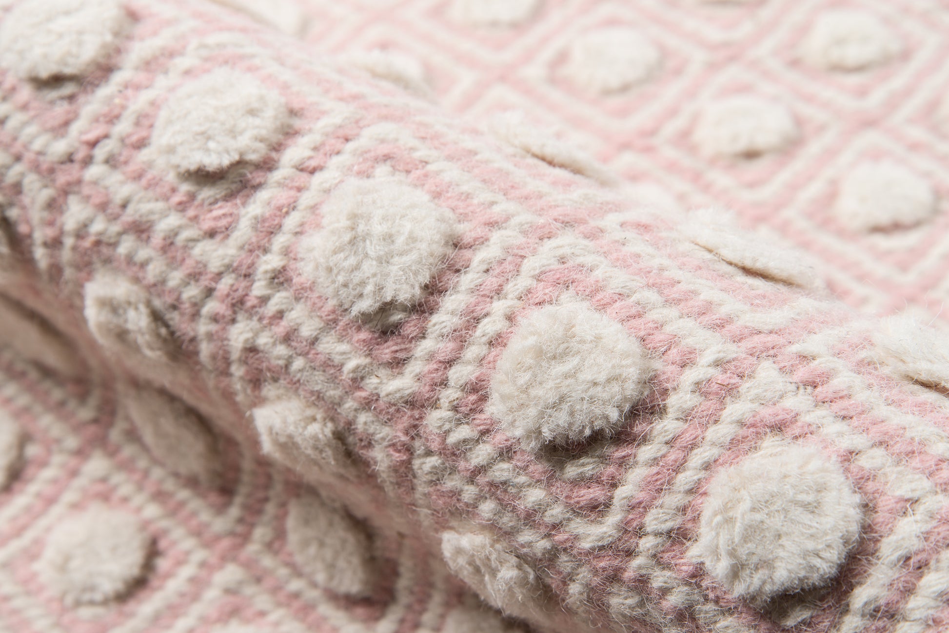 Soft pink rug with cream pom-pom dots and a geometric raised grid pattern.