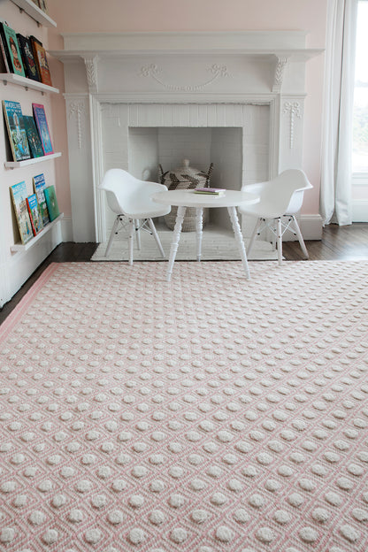 Soft pink textured rug with raised circular dots in a bright, cozy living space, under a white round table with chairs.