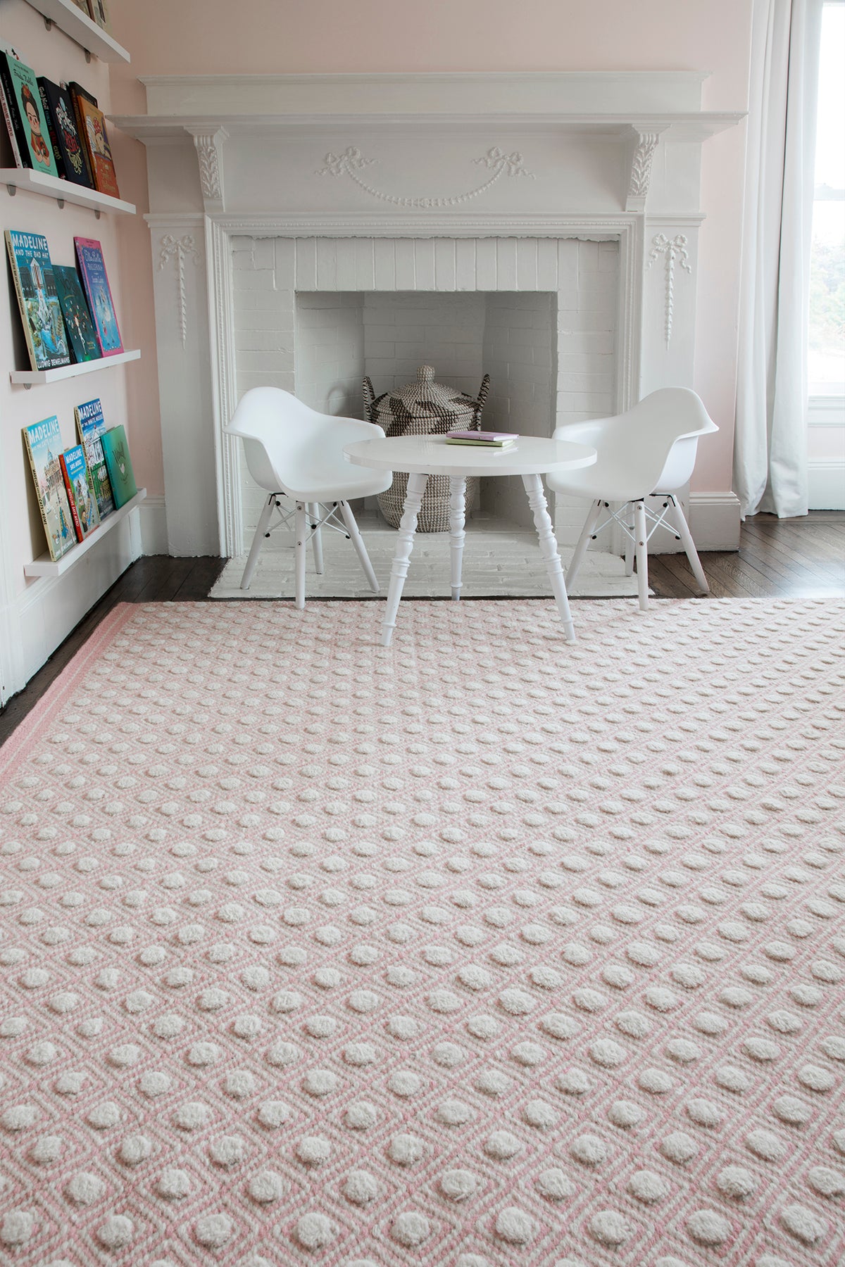 Soft pink tufted rug with white circular bumps in a bright white living room with a round white table and two white chairs.