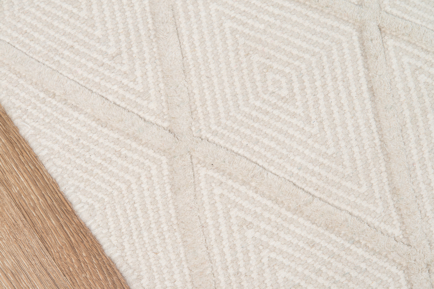 Beige textured rug with white geometric diamond pattern; light wood flooring visible at edge.