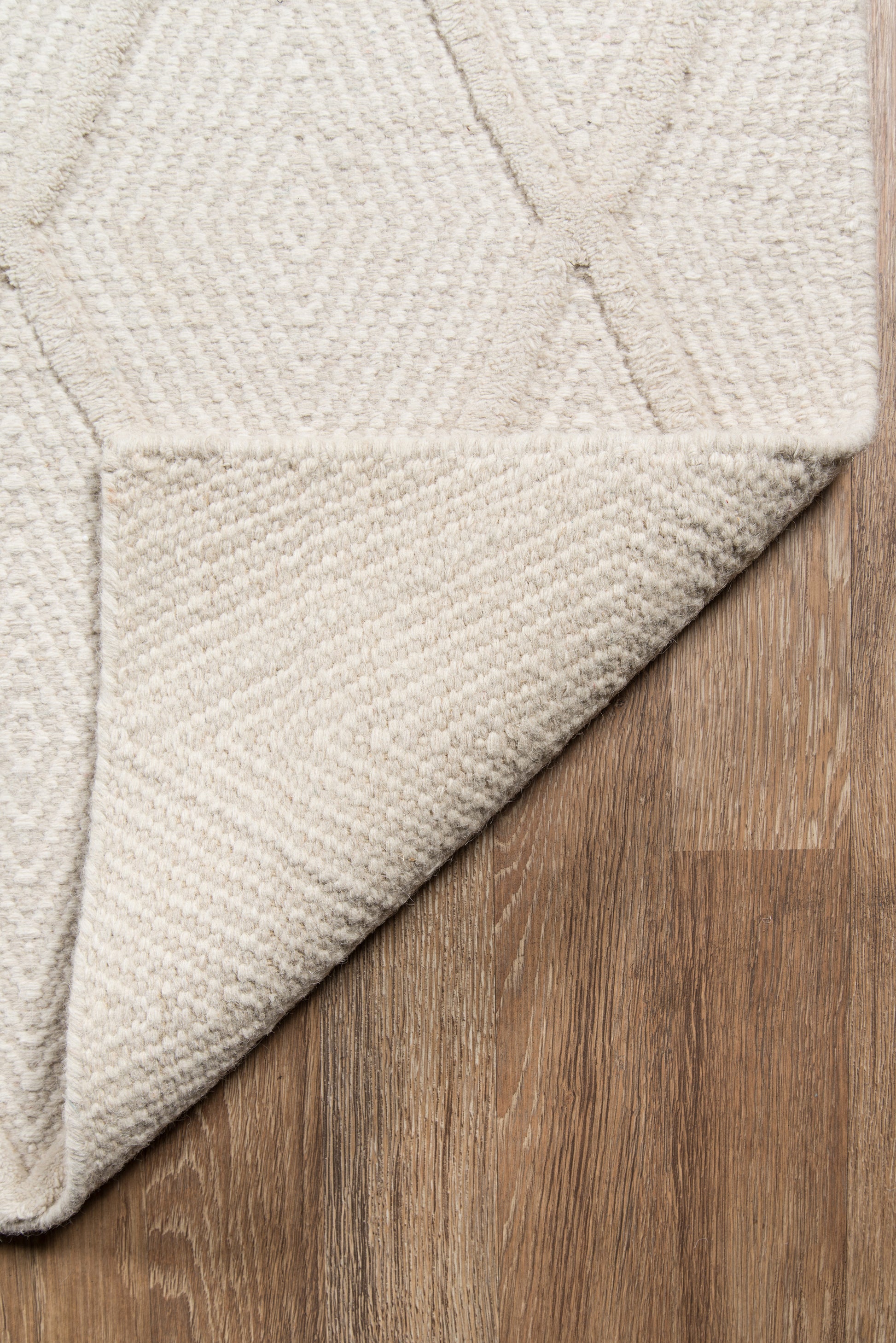 Beige geometric area rug with raised diamond pattern & soft tufted texture, folded corner on wood floor.