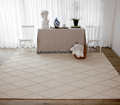 Beige table with linen cloth, bust statue, blue vase, plant and books; white chairs on a diamond-pattern beige rug.