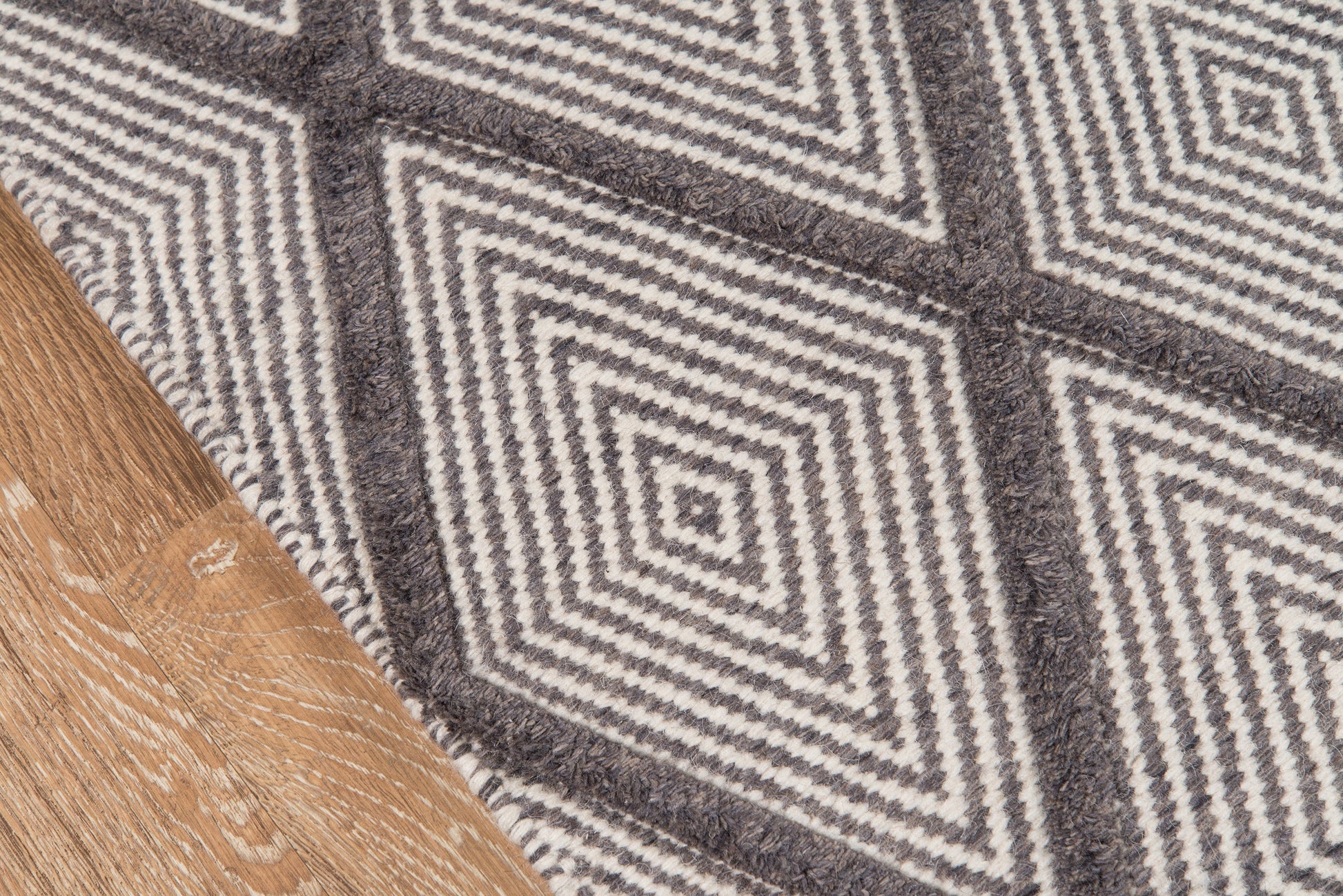 Gray geometric diamond-pattern rug on wood floor; woven textile with white and charcoal lines.