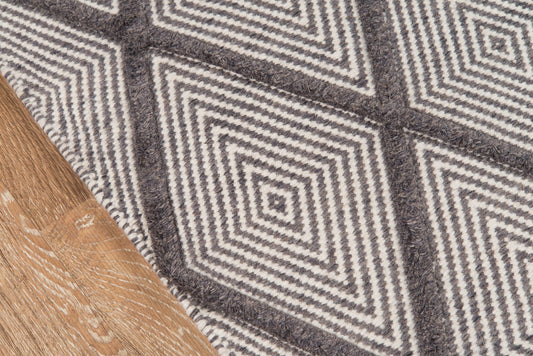 Woven geometric rug in gray and white with diamond pattern on a wooden floor.