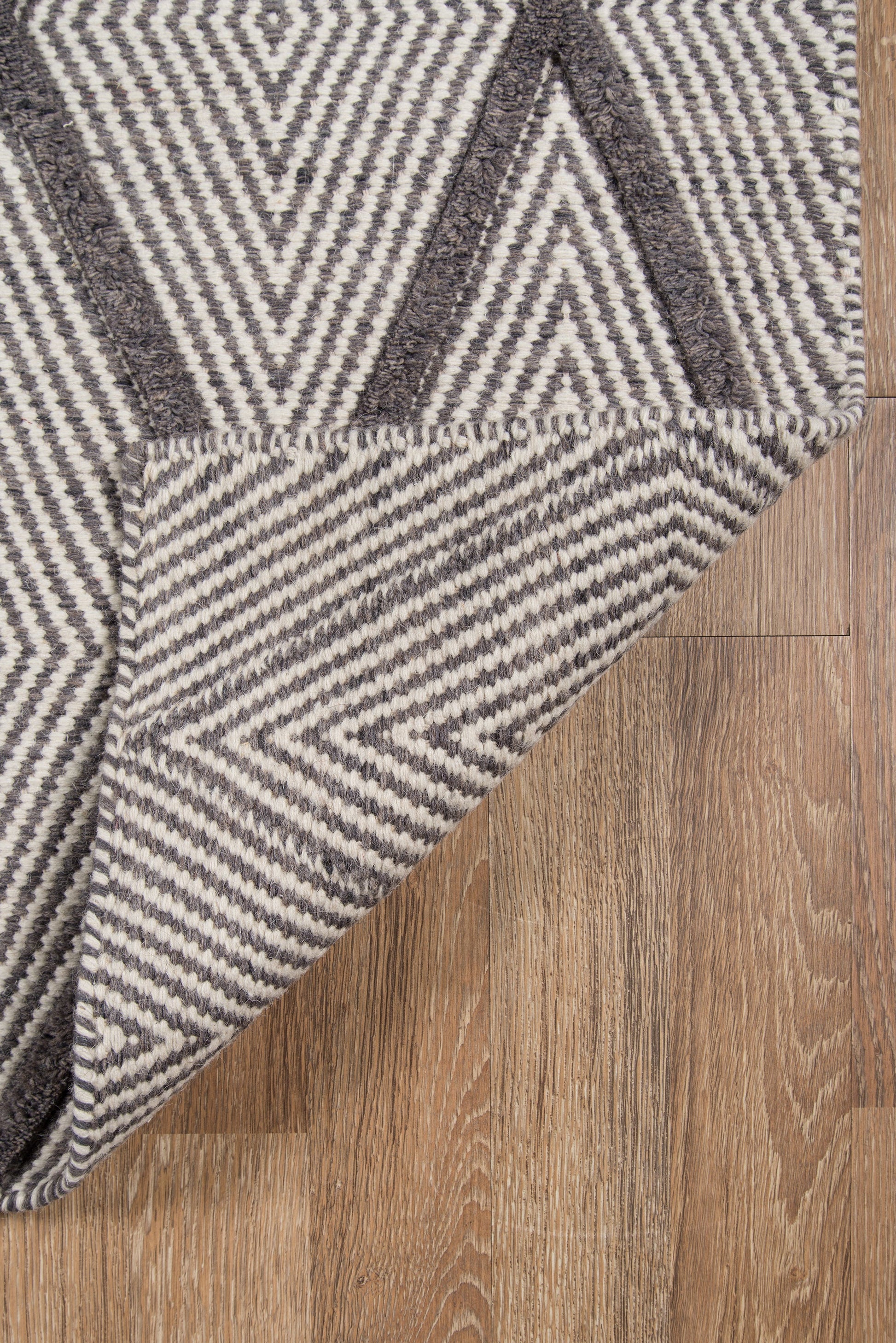 Geometric flatweave rug in gray and ivory with chevron/diamond pattern, folded corner on wood floor.