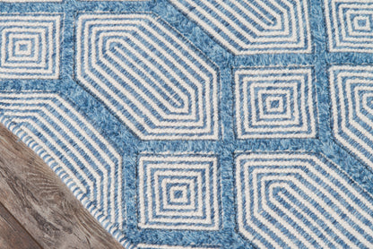 Blue geometric rug with white concentric square spiral patterns, textured pile, corner against a wooden floor.