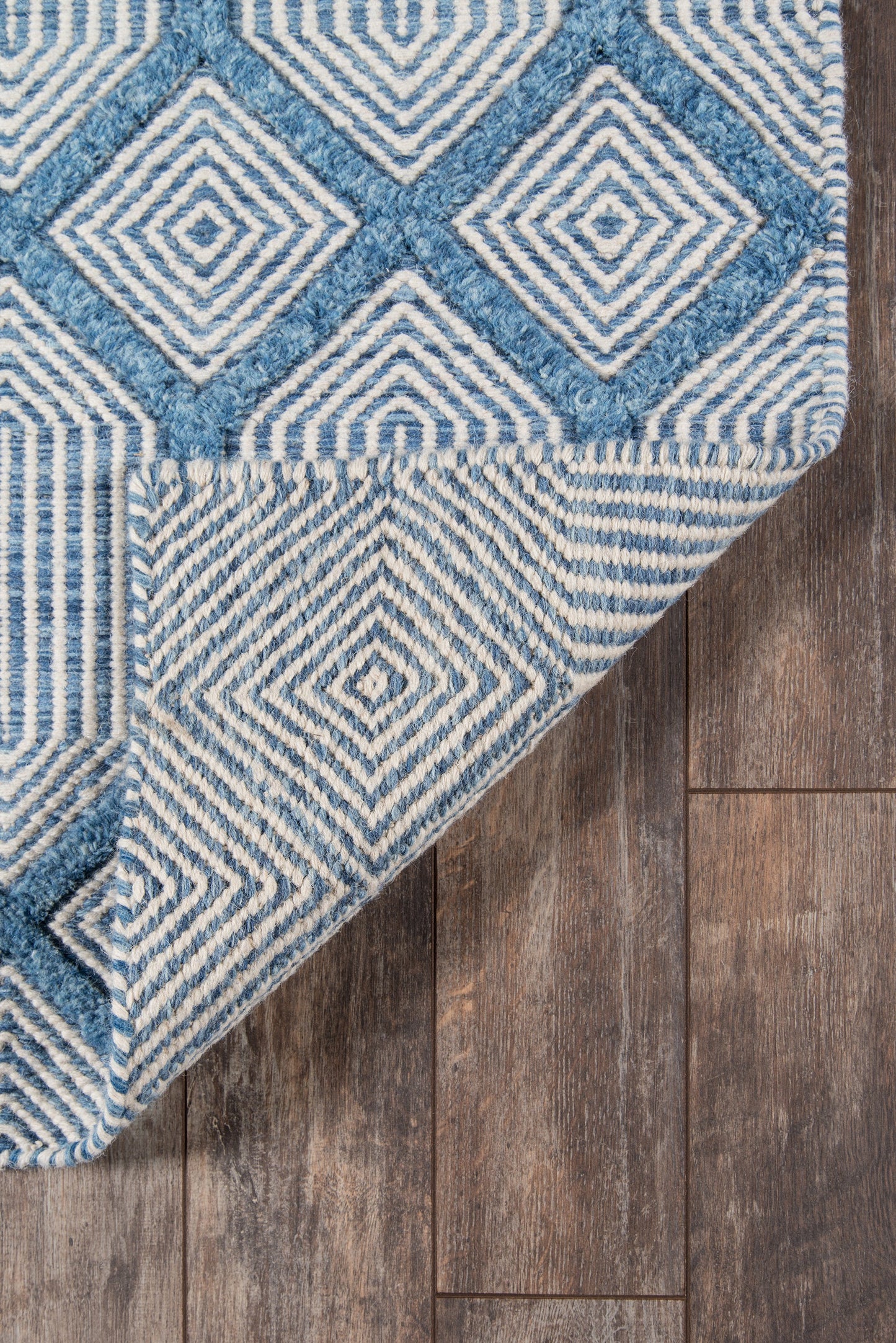 Blue and white geometric rug with concentric diamond patterns, tufted, on dark wood floor.