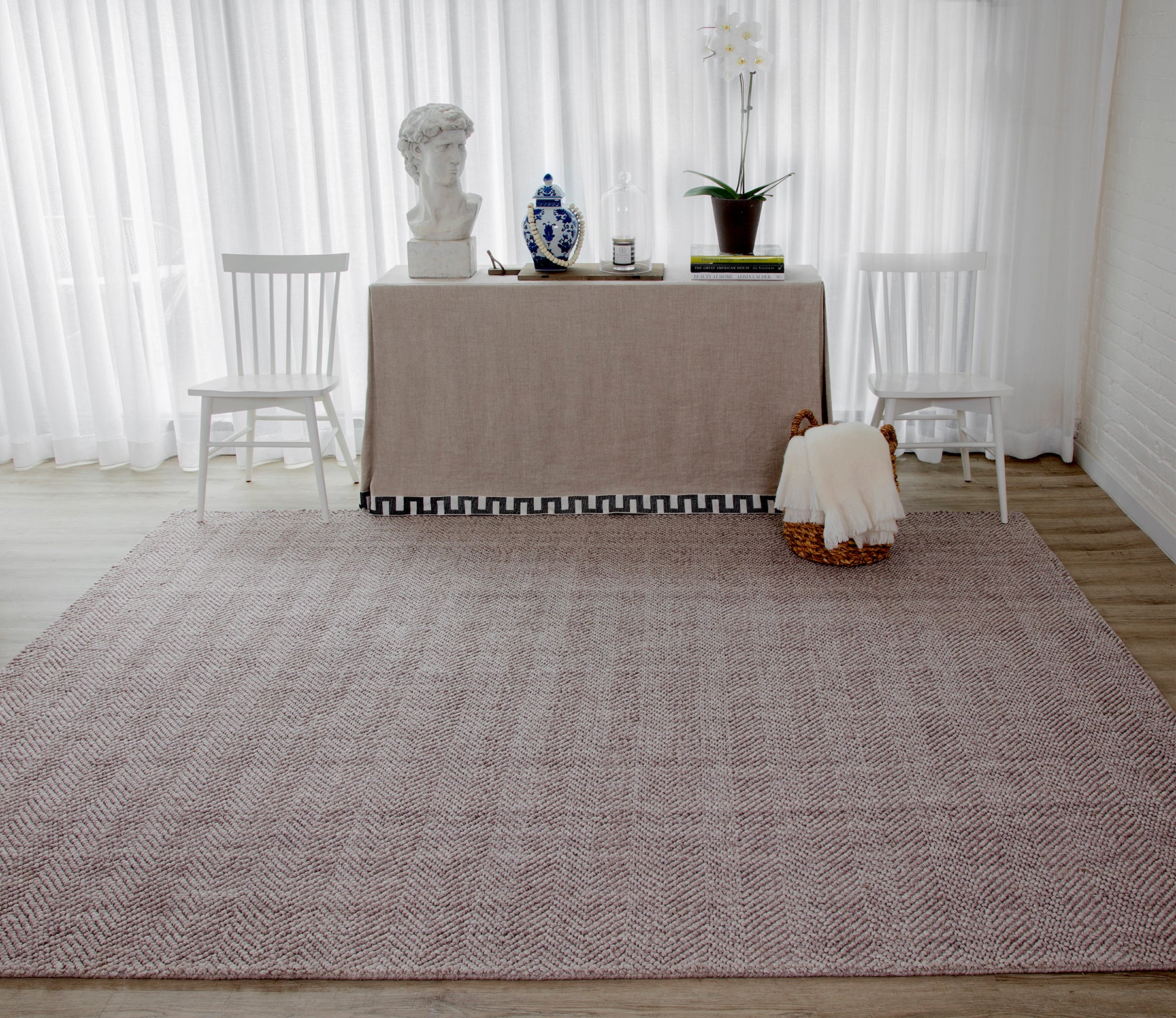 Rectangular neutral beige-brown textured woven runner rug on light wood floor; paired with a linen-covered table and white chairs.