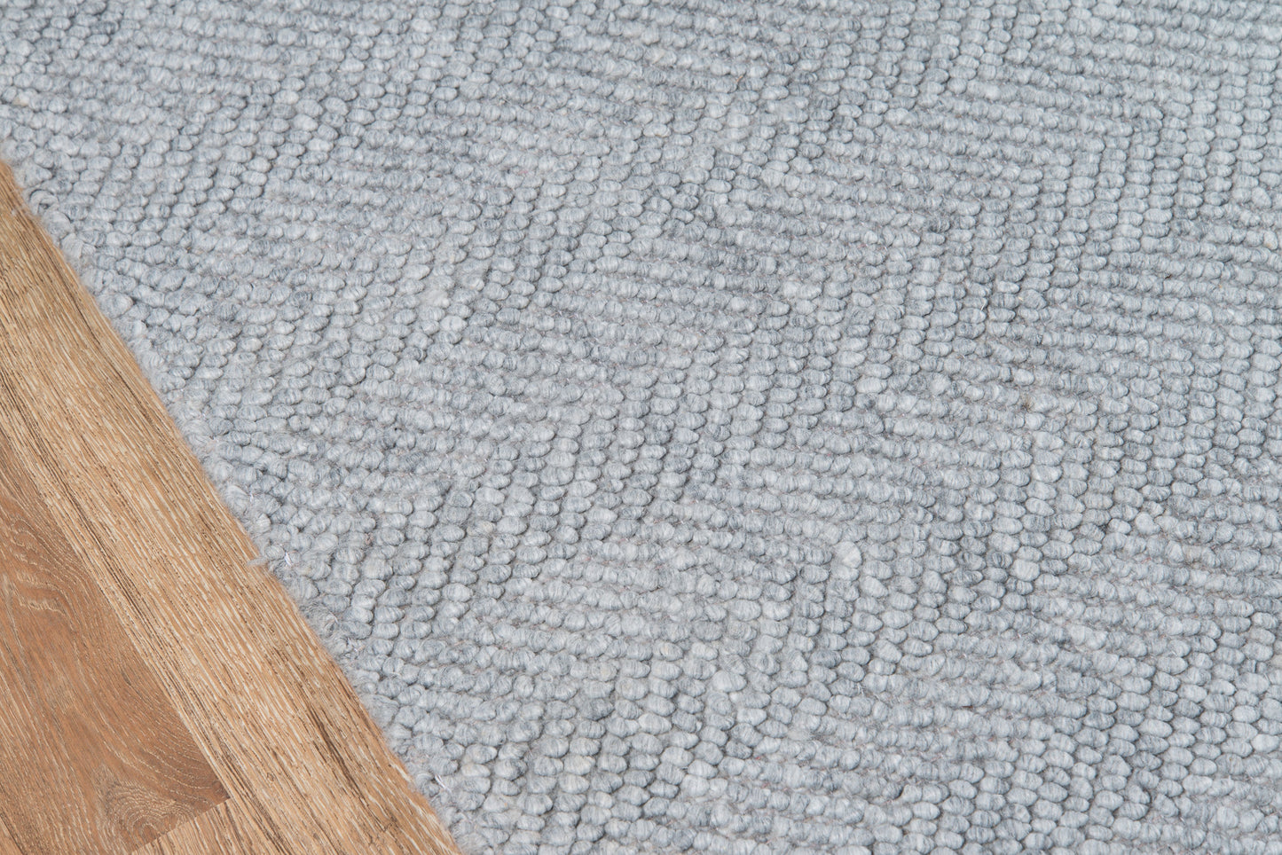 Light gray textured rug with a looped pile beside a wooden floor edge.