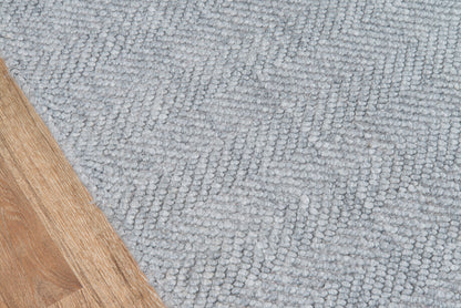 Light gray textured rug with a looped pile beside a wooden floor edge.