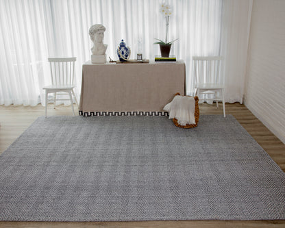 Rectangular gray woven area rug on light wood floor in a minimalist dining setup with white chairs and a beige-draped table.