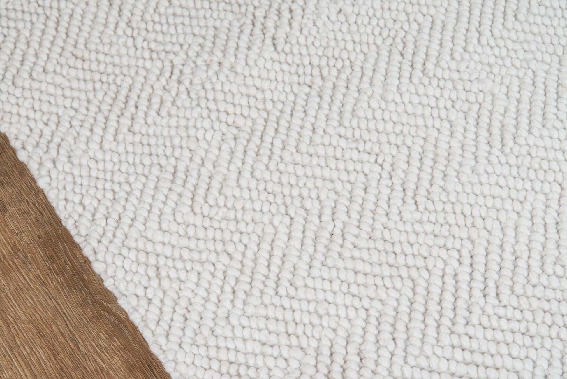 White looped-pile rug with chunky fibers on natural wood floor.