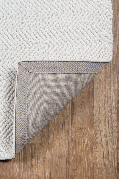 Cream shag rug with dense loop pile; folded corner reveals gray fabric underside with striped edge on wood floor.