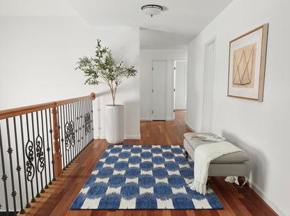 Bright hallway with blue and cream geometric rug, beige bench, white ribbed planter with tall plant, decorative iron railing.