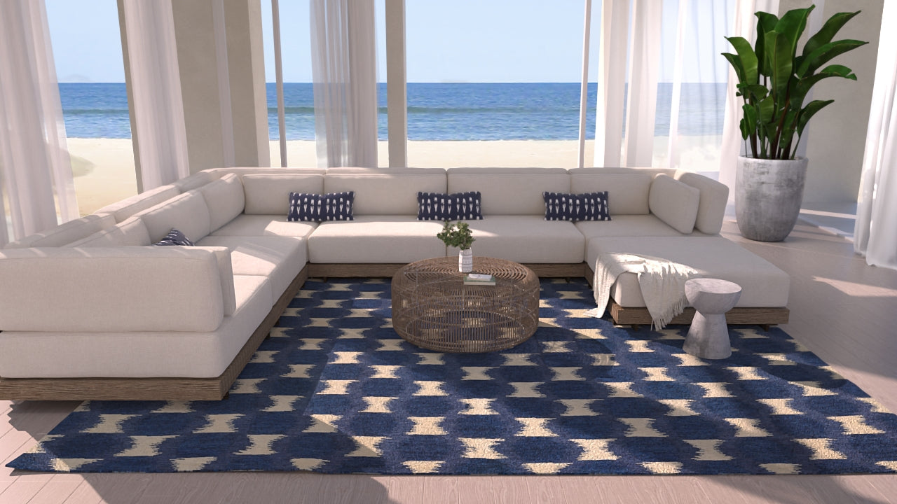 Coastal living room with white sectional, round wicker coffee table, blue-and-white geometric rug, navy pillows, and ocean view