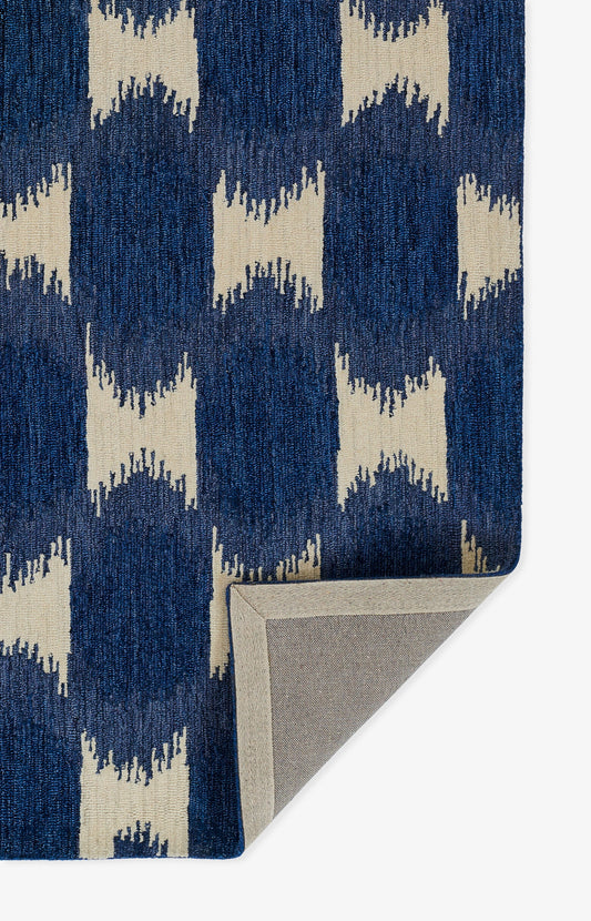 Navy rug with cream geometric blocks in a repeating pattern; woven texture, corner folded to reveal gray backing.