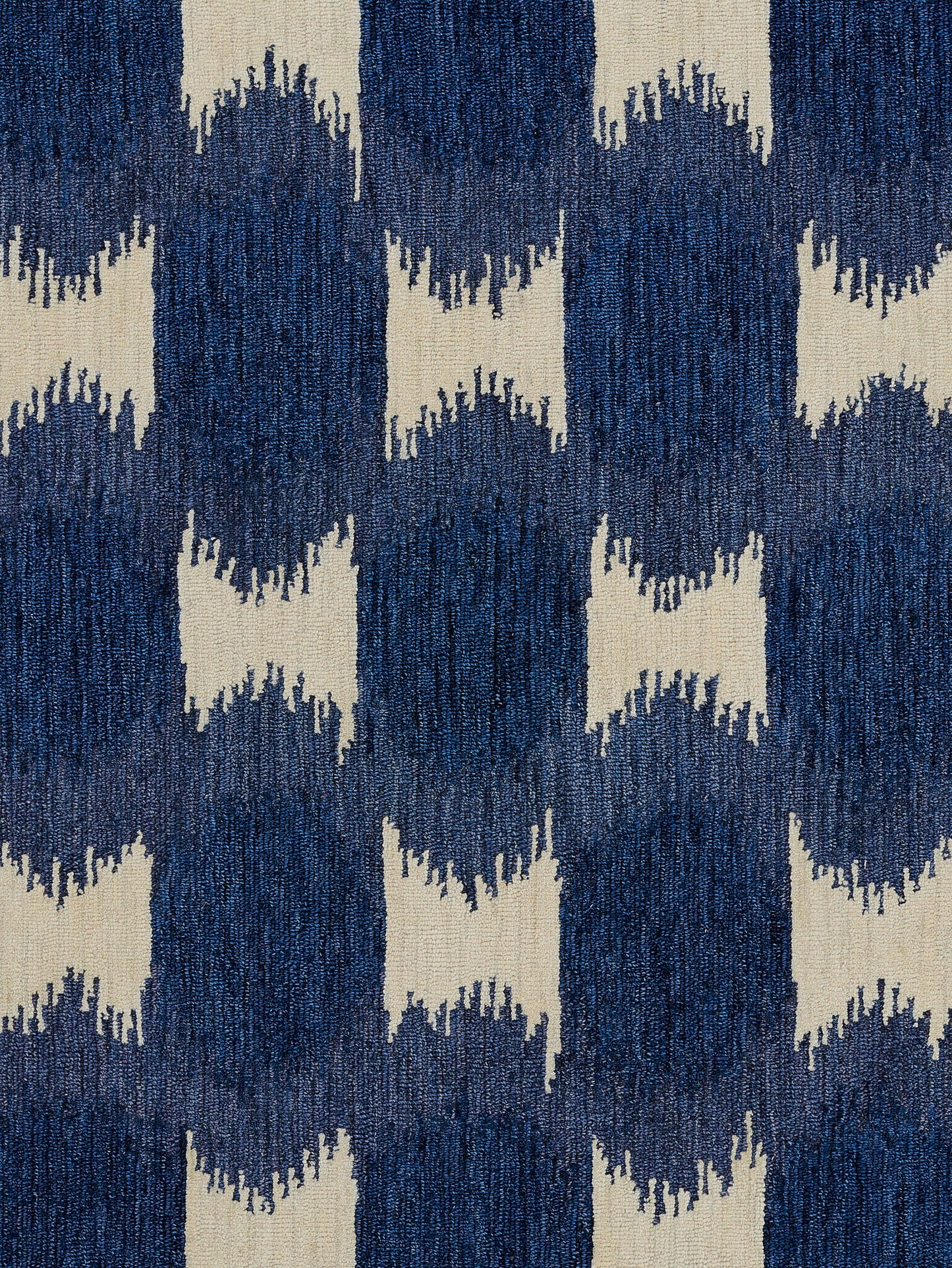 Woven rug in navy and cream with ikat-inspired zigzag geometric blocks; bold floor decor.