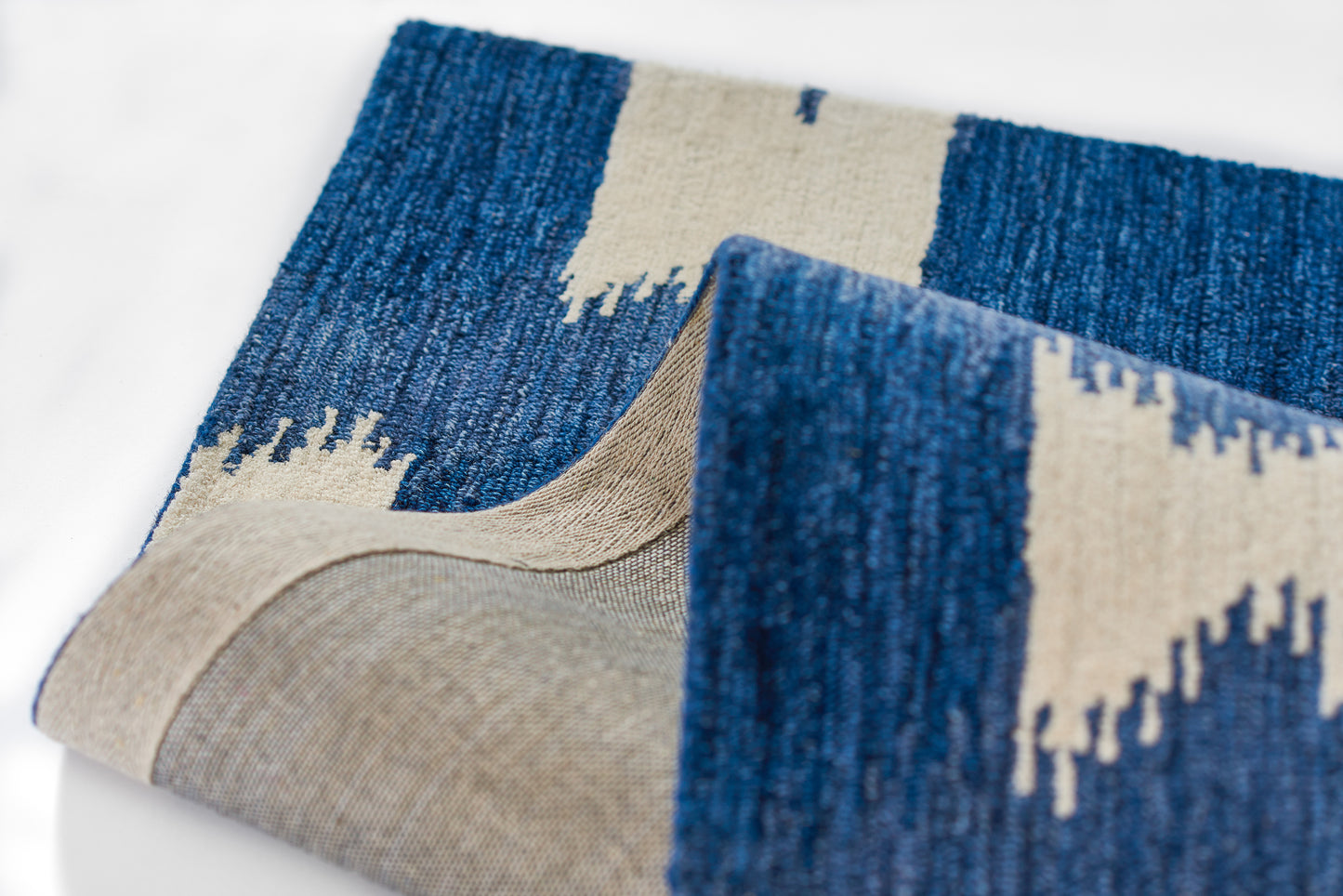 Blue and beige geometric woven rug with zigzag pattern, kilim-style, folded to reveal thick textured textile.