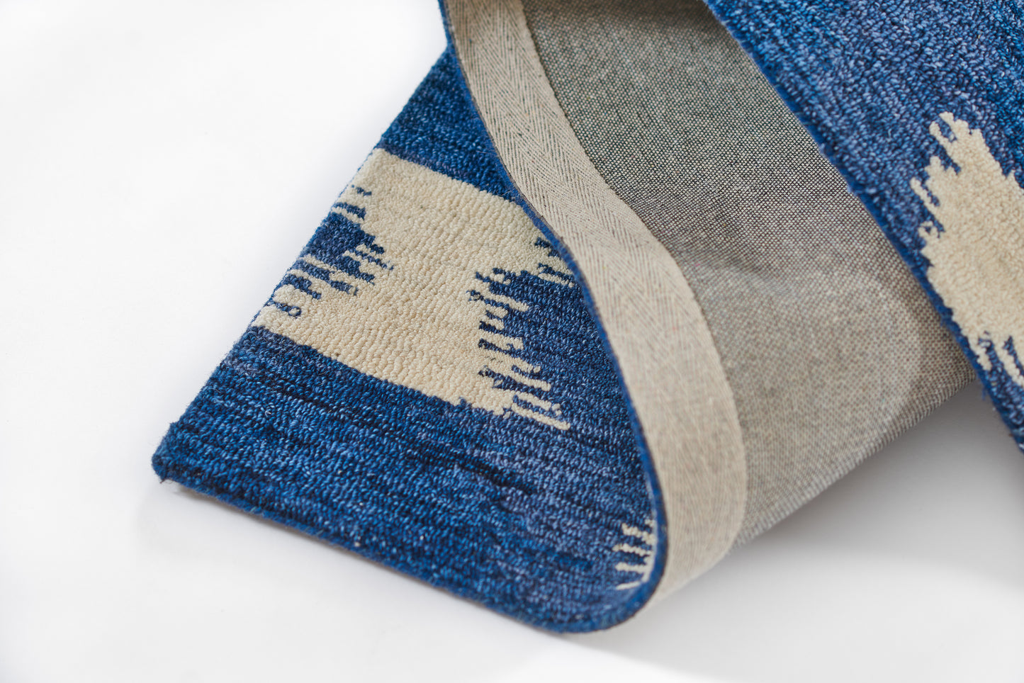 Blue woven runner rug with beige and gray geometric pattern, folded edge showing reverse side, 3' x 8'.