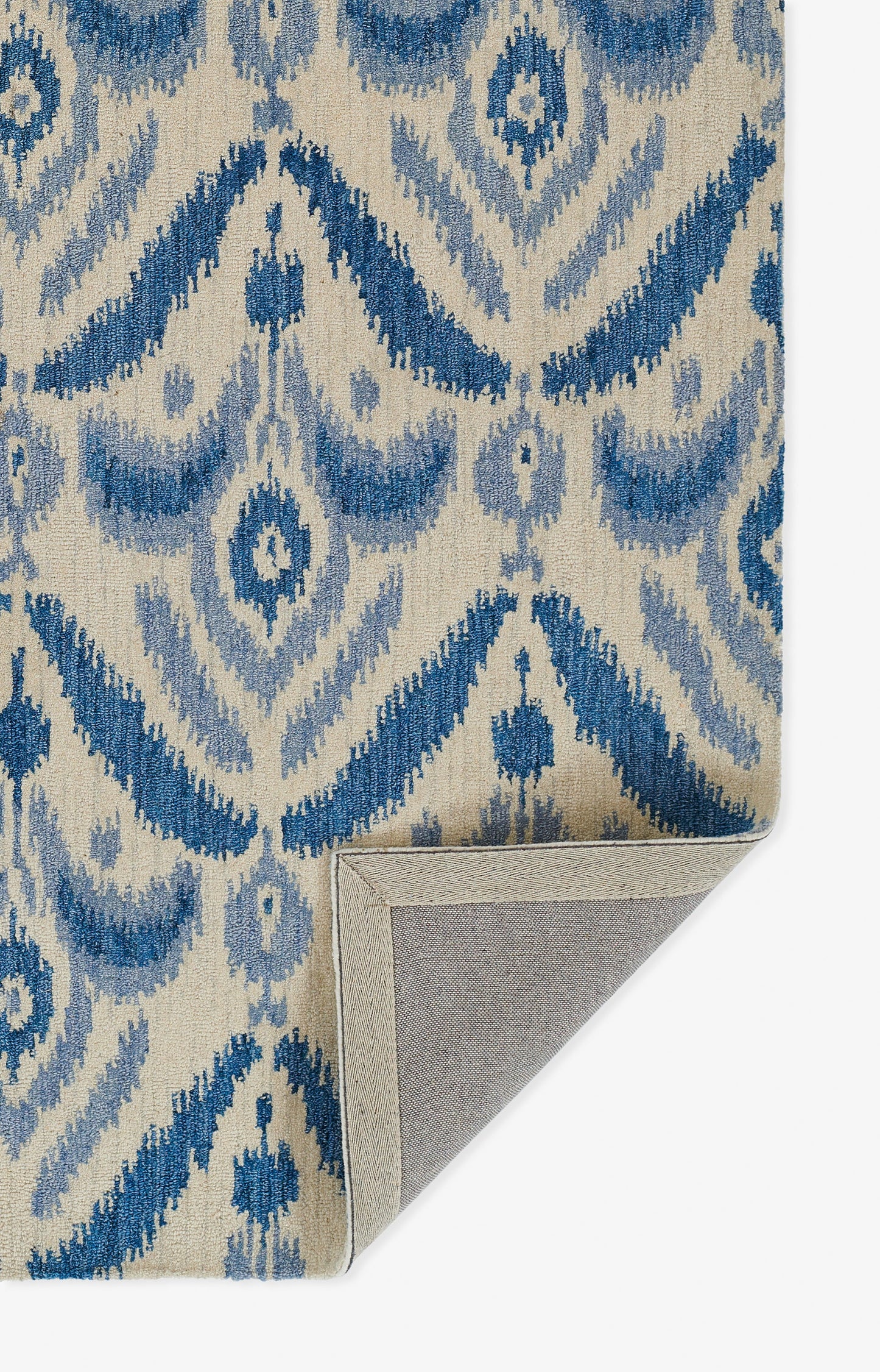 Blue & beige Ikat-patterned rug with diamond motifs; woven texture, folded corner showing gray backing.