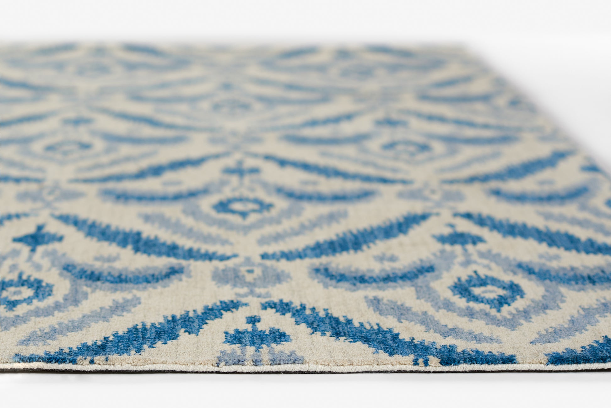 Blue and beige patterned rug with ornate damask motifs in a woven texture, close-up view.