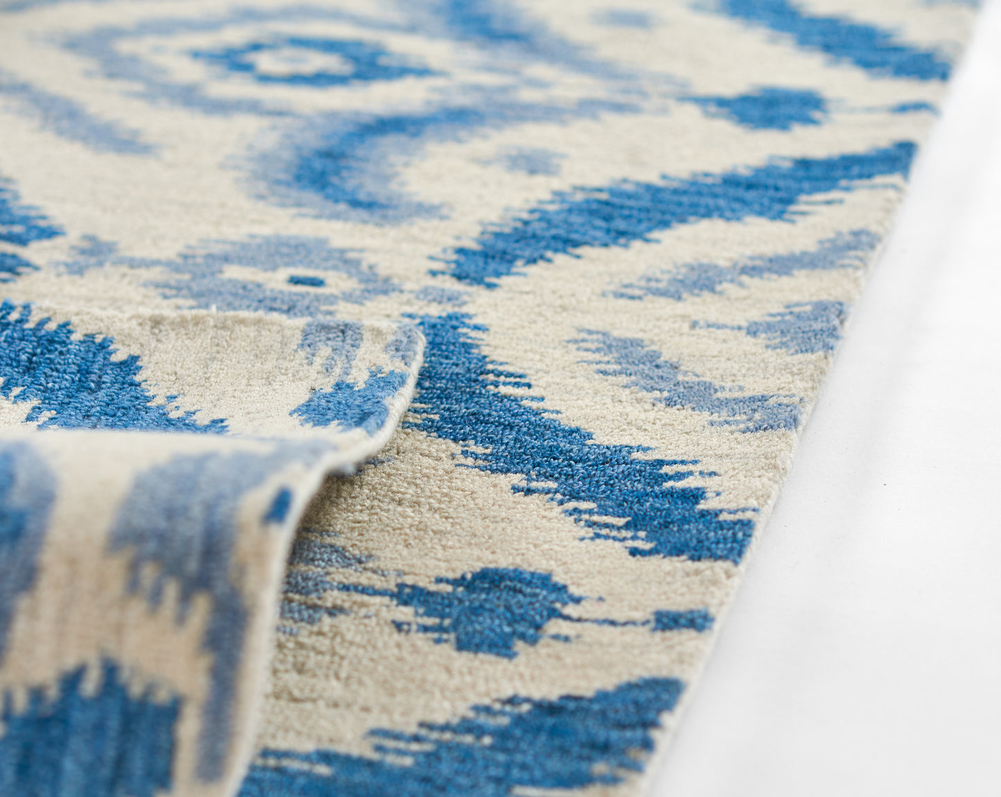 Blue and beige ikat-style geometric rug with soft textured pile and folded corner.
