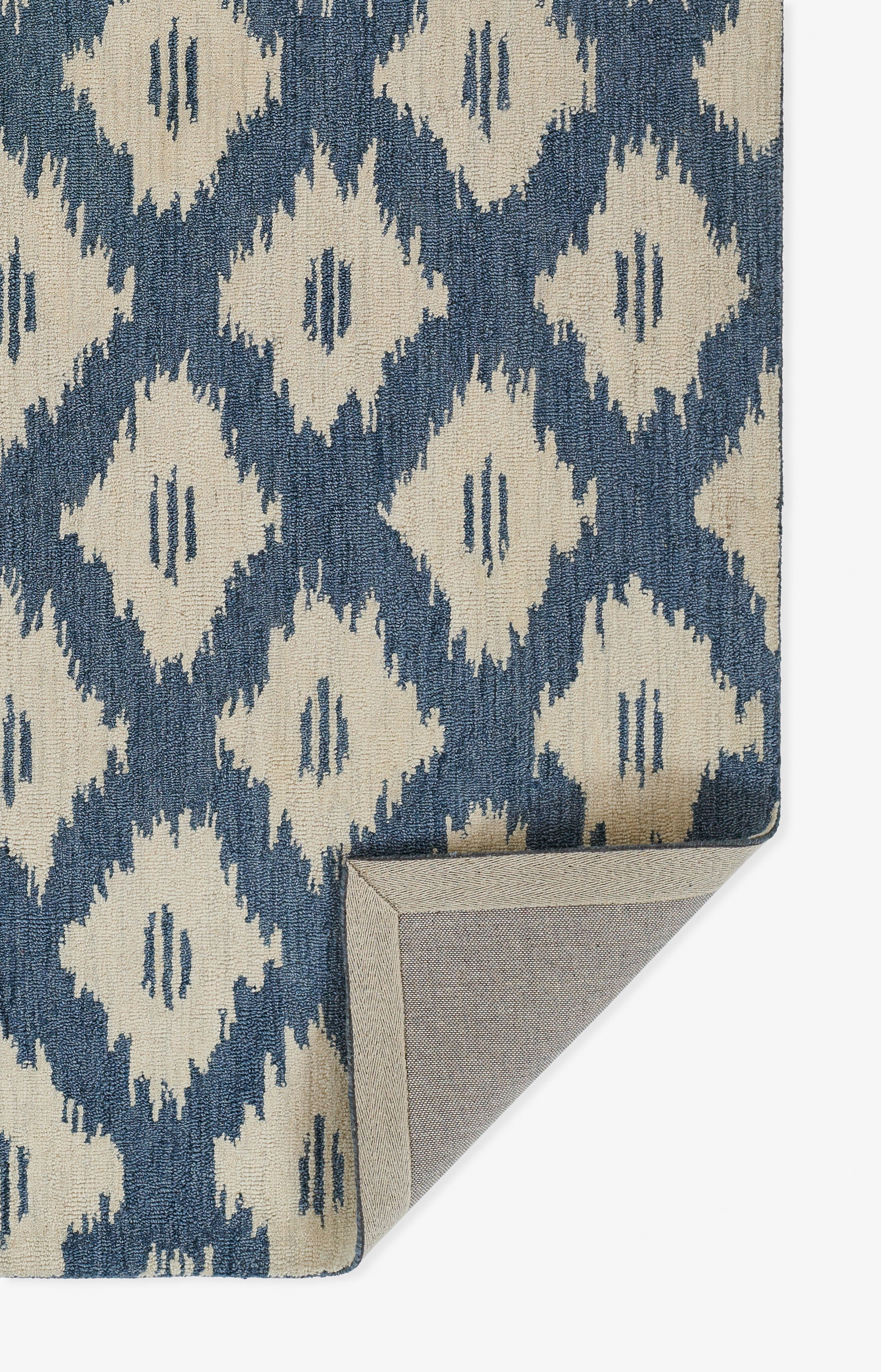 Blue and beige ikat rug with geometric diamond motif; rectangular, woven texture, corner folded showing tan underside.