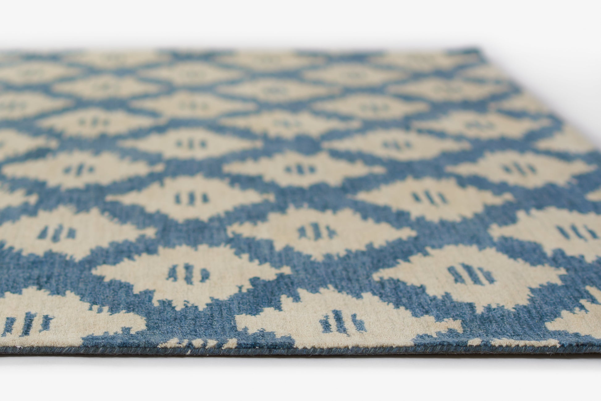 Blue and beige geometric rug with diamond lattice pattern; woven textile with soft texture.
