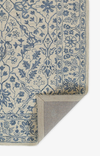Blue floral on beige rug with ornate border; traditional oriental style, corner folded to show the backing.