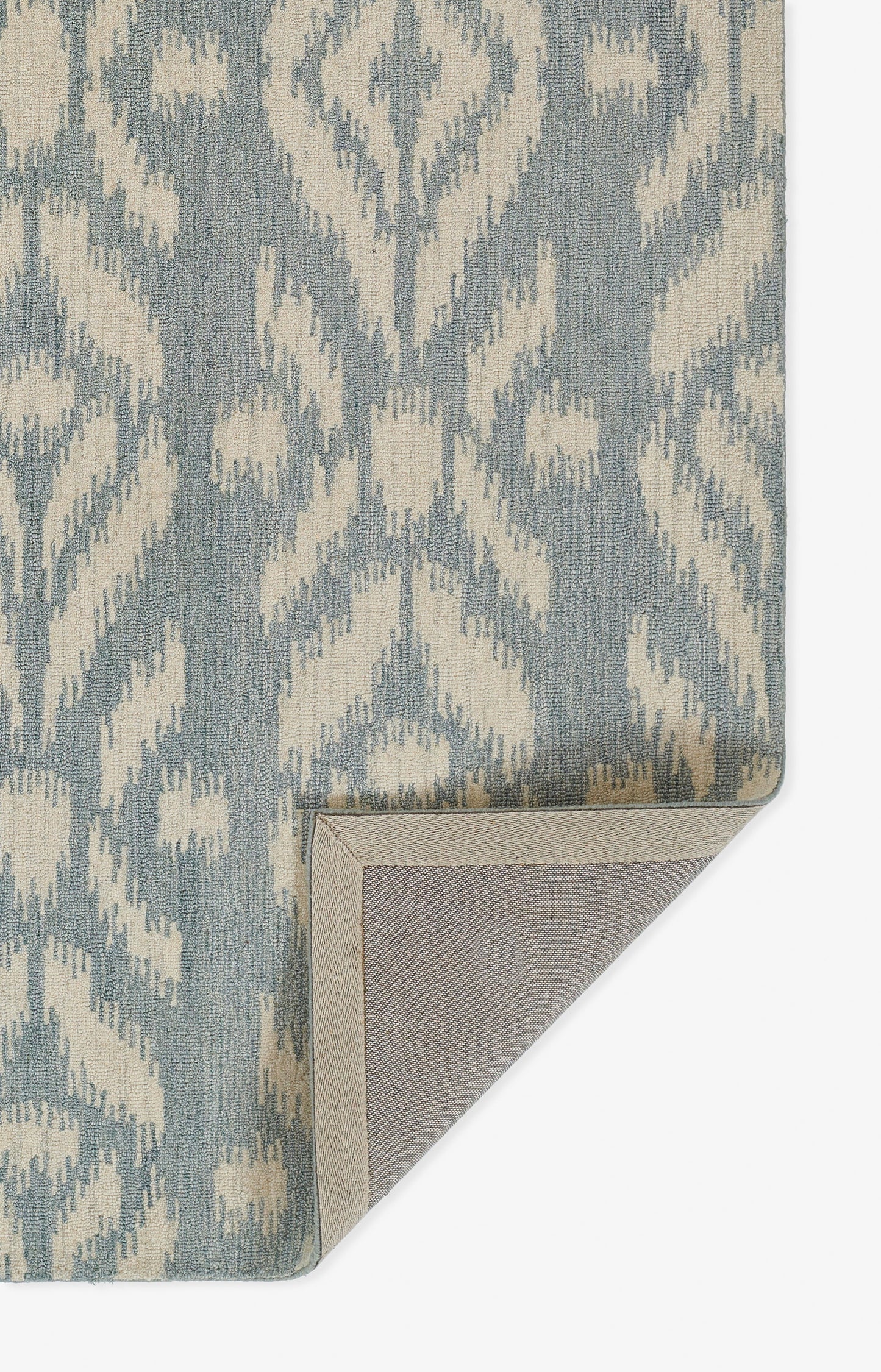 Blue-gray and ivory ikat-inspired woven rug with damask pattern; folded corner reveals the underside.