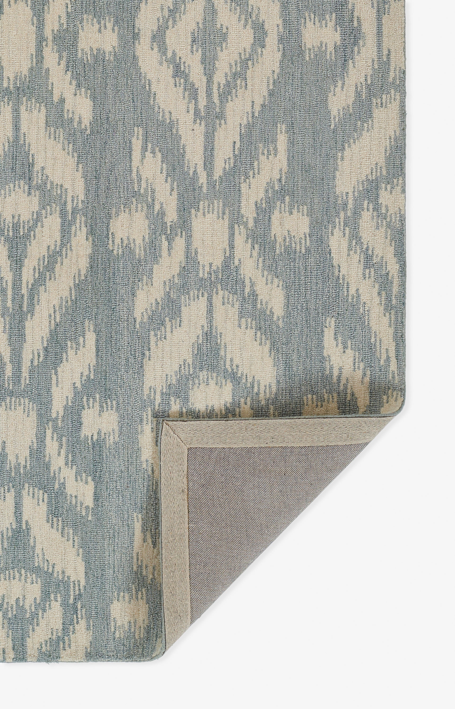 Blue-gray and cream ikat patterned rug with woven texture; corner folded to reveal beige backing.