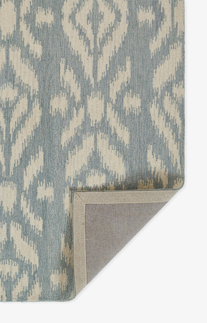 Blue-gray and cream ikat patterned rug with woven texture; corner folded to reveal beige backing.
