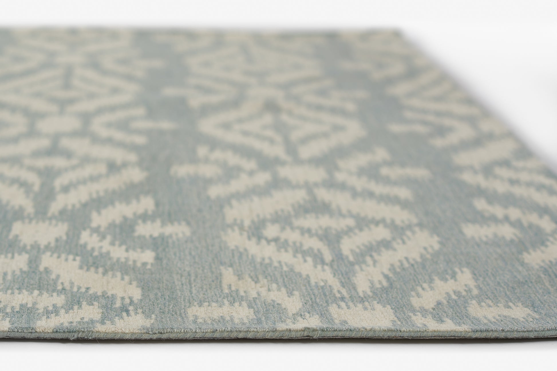Blue-gray flat-weave rug with ivory geometric ikat pattern, rectangular, modern coastal style.