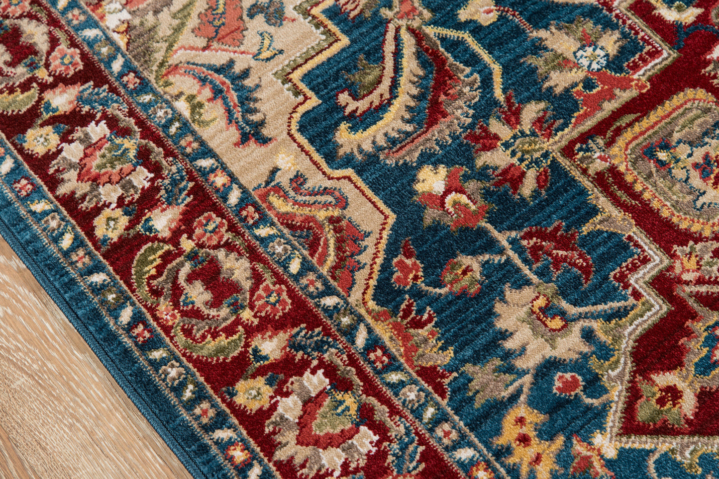 Blue oriental area rug with red & beige borders, intricate floral medallion motifs on a wooden floor.