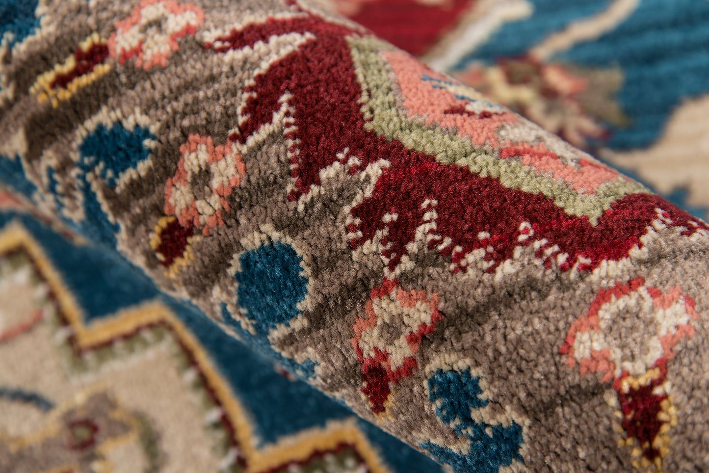 Close-up of a rolled oriental rug with plush pile; blue, red, beige and gray geometric motif.