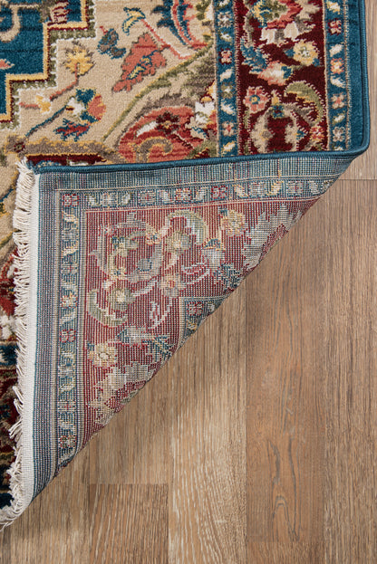 Blue-toned oriental area rug with floral border; folded corner reveals pinkish-blue underside; wood floor.