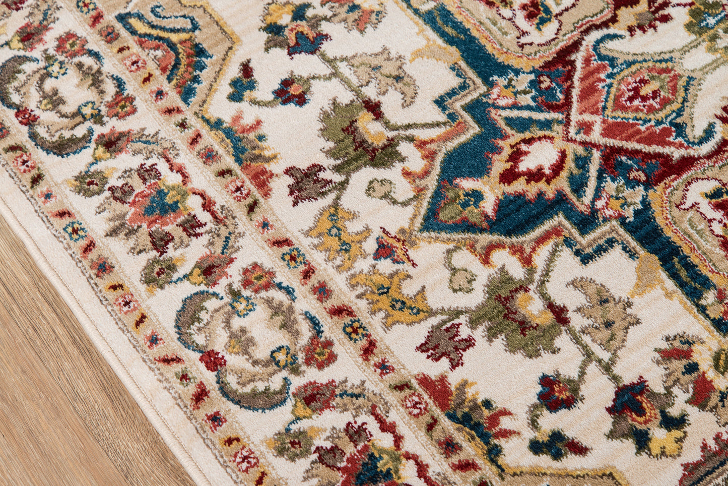 Rectangular woven oriental rug with ivory base and multicolor red, blue, green, and gold floral motifs on a light wood floor.