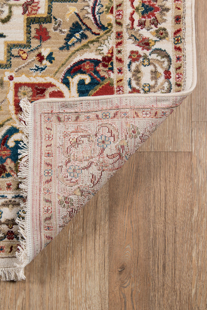 Persian-inspired area rug with red, blue & beige motifs, fringed edges, partially flipped over on a wooden floor.