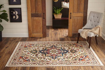 Cream oriental rug with blue, red and gold motifs on a dark wood hallway floor, flanked by double doors and a gray upholstered chair