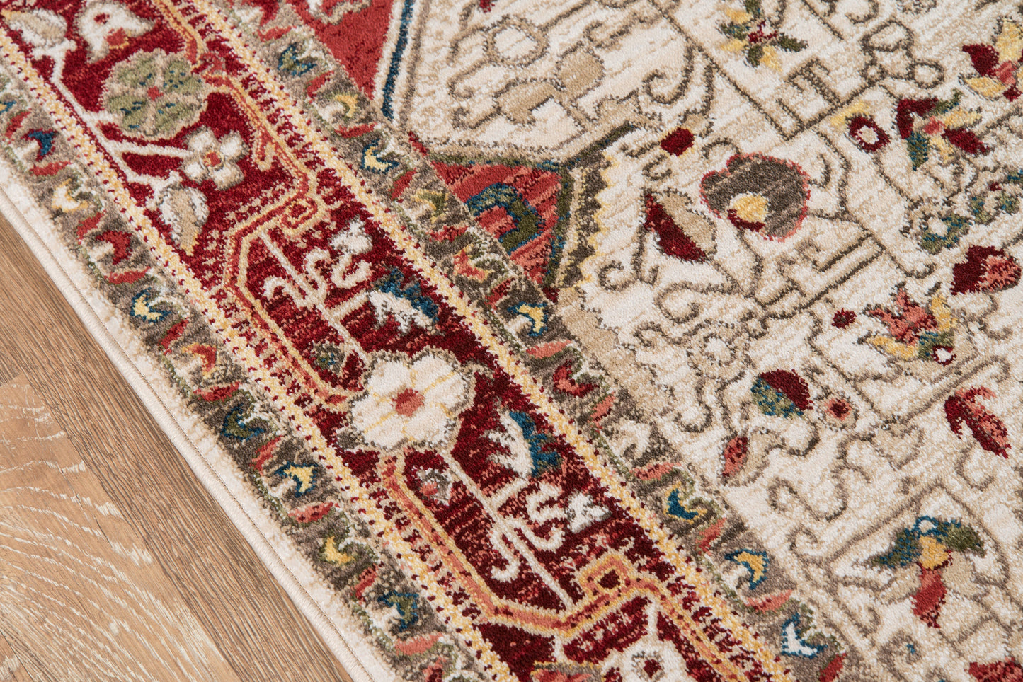 Oriental wool rug with ivory center and red border, floral motifs, on wooden floor.