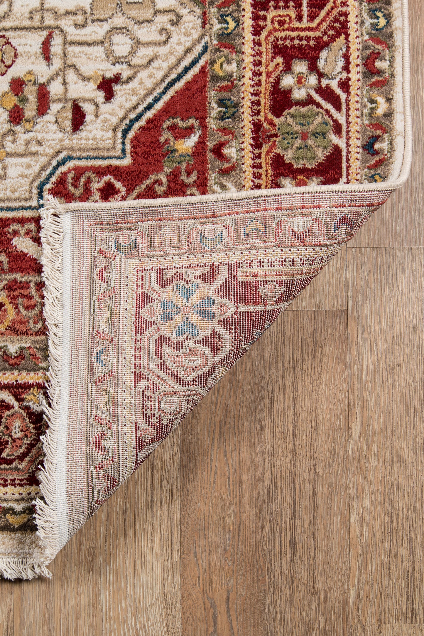 Persian-inspired red and ivory area rug with floral motifs, fringed edges, folded to reveal backing on a wood floor.