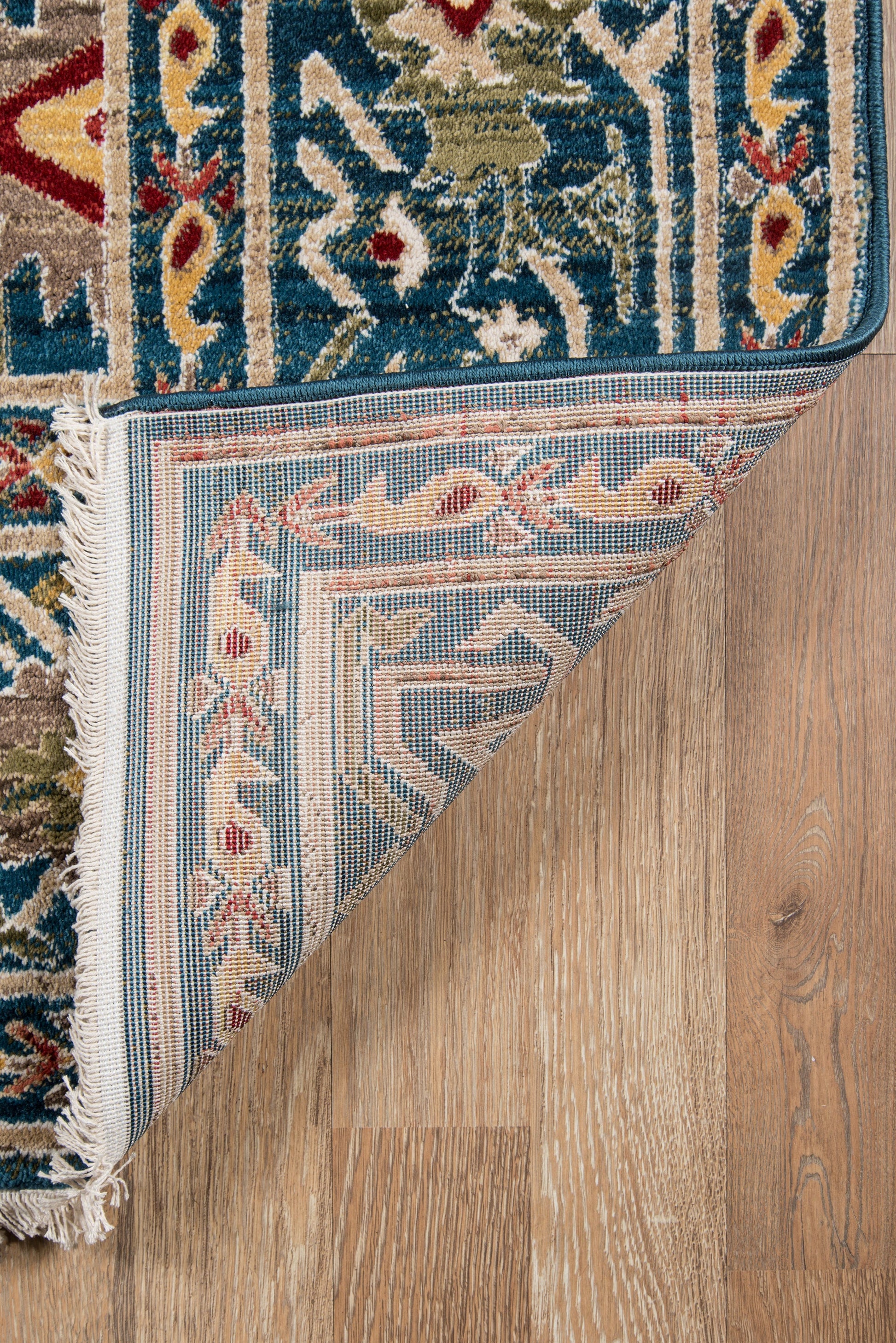 Blue and ivory Persian-style area rug with red accents, fringed edges, folded corner on wood floor.