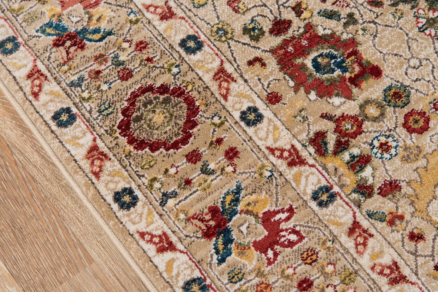 Ivory-beige oriental rug with red, blue and yellow floral motifs and an ornate border on a wooden floor.