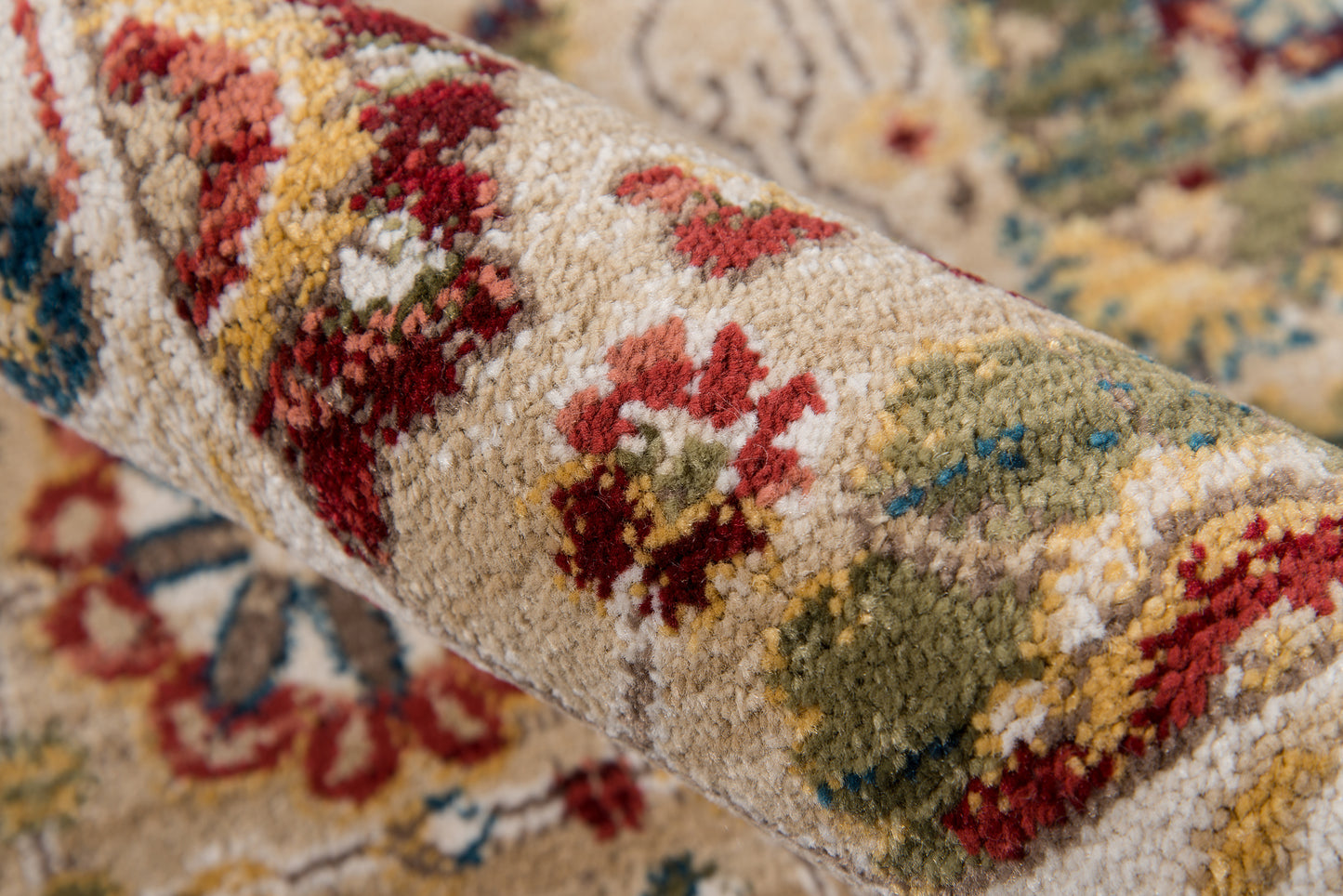 Close-up of a rolled oriental rug with a cream background and multicolor floral motifs in red, green, and blue; plush pile.