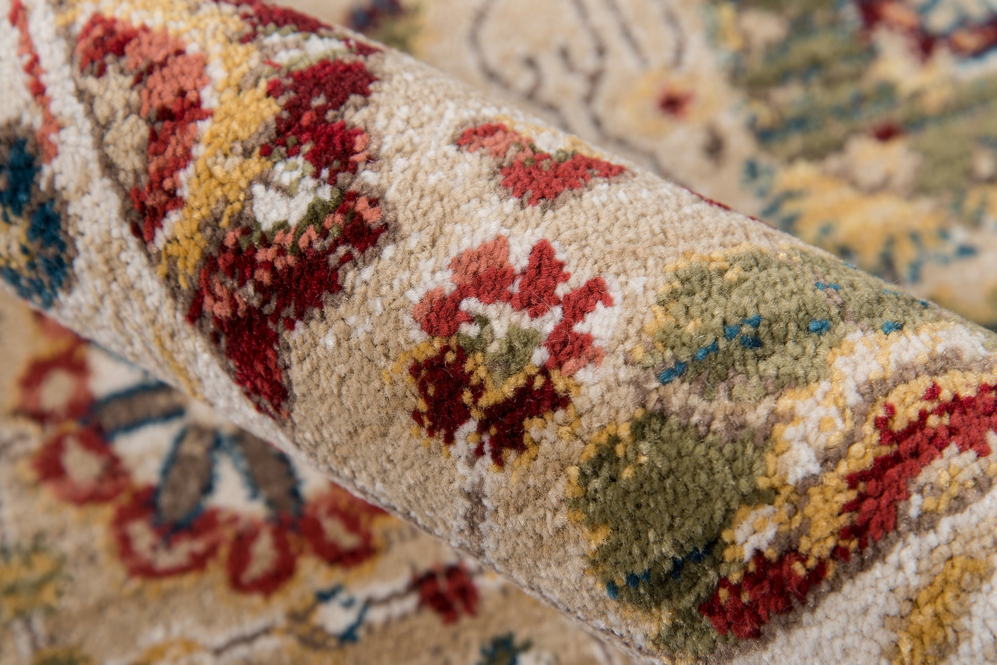 Close-up of a rolled oriental rug with a cream background and multicolor floral motifs in red, green, and blue; plush pile.